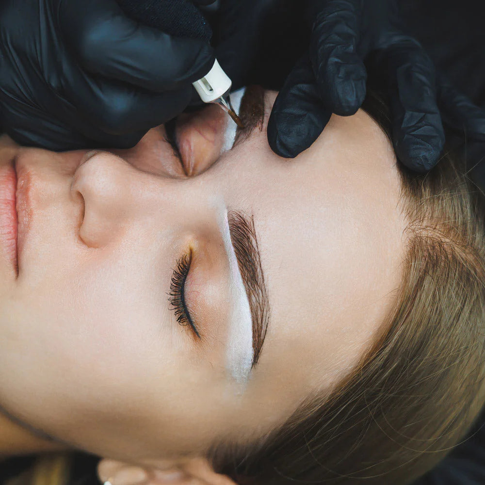 Eyebrow tattoo process with a professional in black gloves.