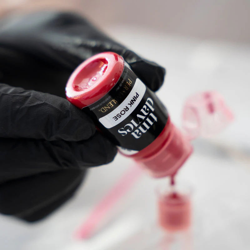 Pink nail polish bottle with a gloved hand holding it, on a blurred background