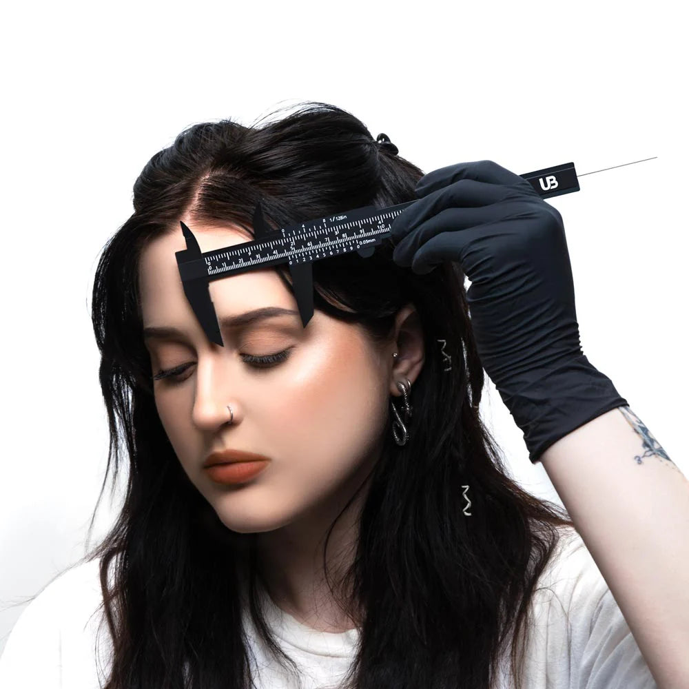 Person with black gloves using a hair-styling tool on their head against a white background